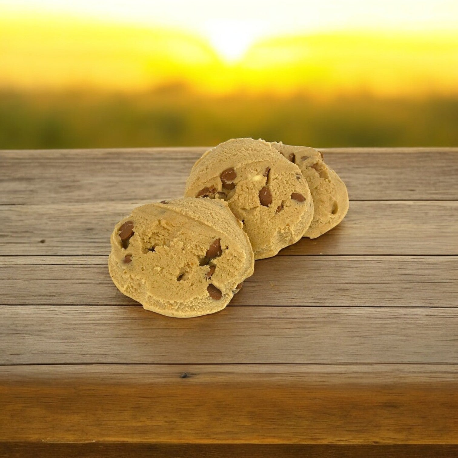 Three peanut butter cookies, made with David's Cookies Dough, rest on a wooden surface against a blurred sunset.