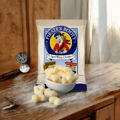 A bag of Pirate's Booty Aged White Cheddar Puffs .5 oz Bag sits on a wooden surface, with some puffs in a small white bowl in front of it.