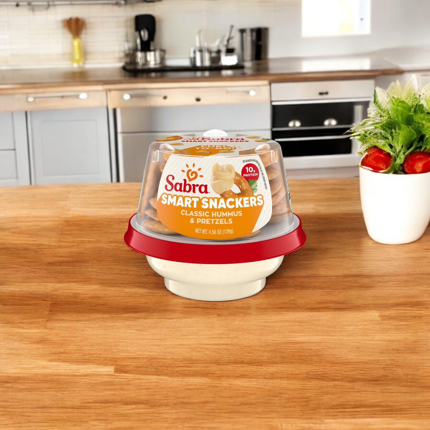 A package of Sabra Classic Hummus with Pretzels, 12 Pack, 4.56 oz each, sits on a wooden kitchen counter in a modern kitchen, offering a savory snack option.