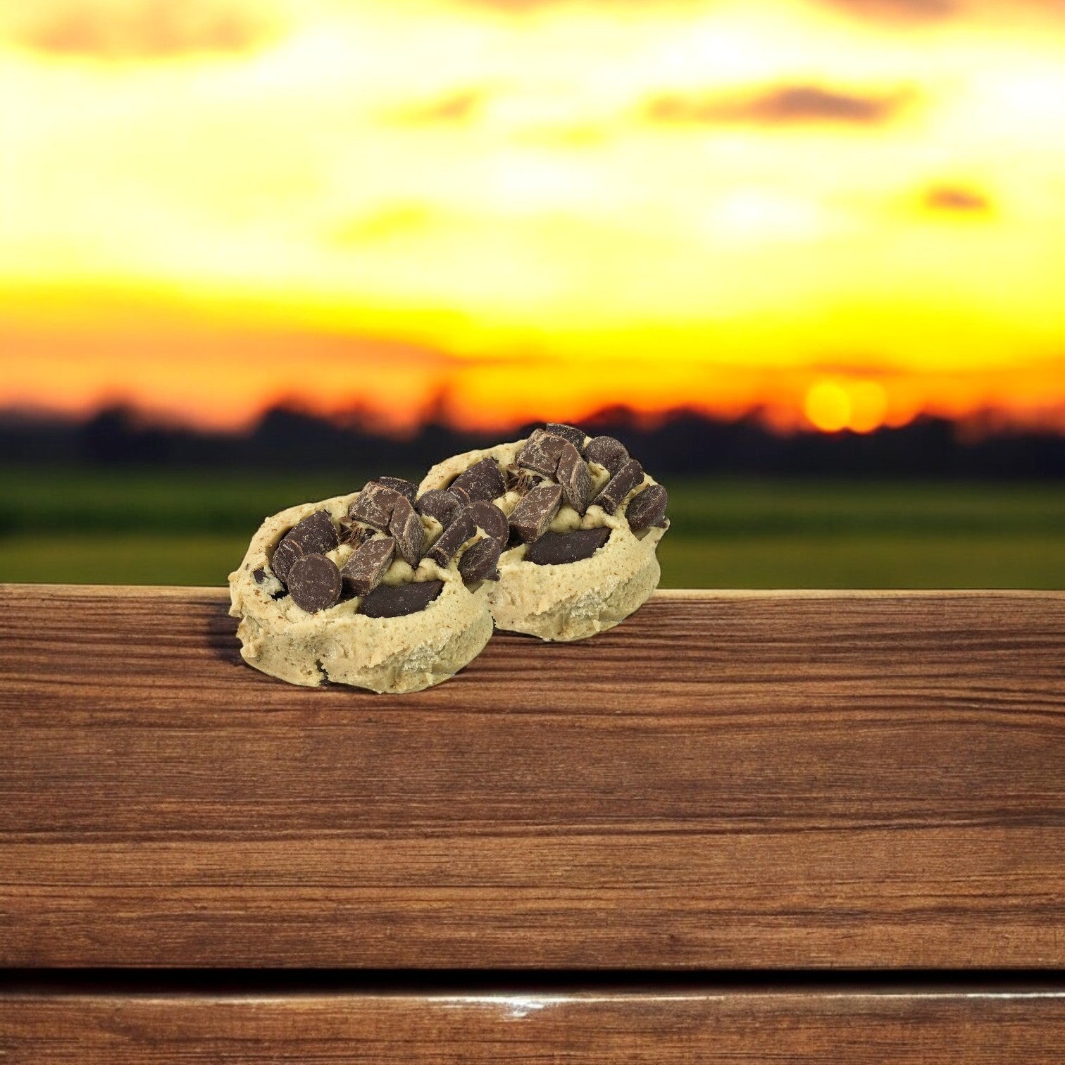 Two of David's Cookies Dough Triple Chocolate cookies sit on a wooden ledge as the sunset creates a warm backdrop, offering a delightful treat for chocolate lovers.