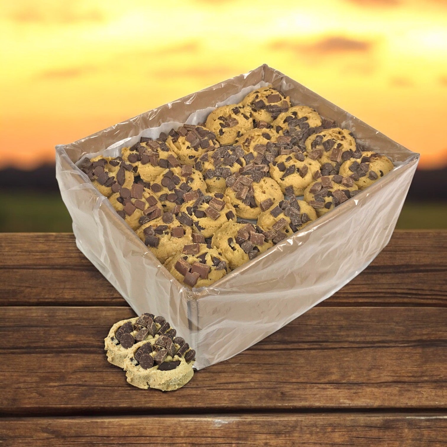 A box of David's Cookies Triple Chocolate cookies rests on a wooden surface, accompanied by two enticing treats. In the background, a blurred sunset creates the perfect ambiance for chocolate lovers to savor these rich delights.