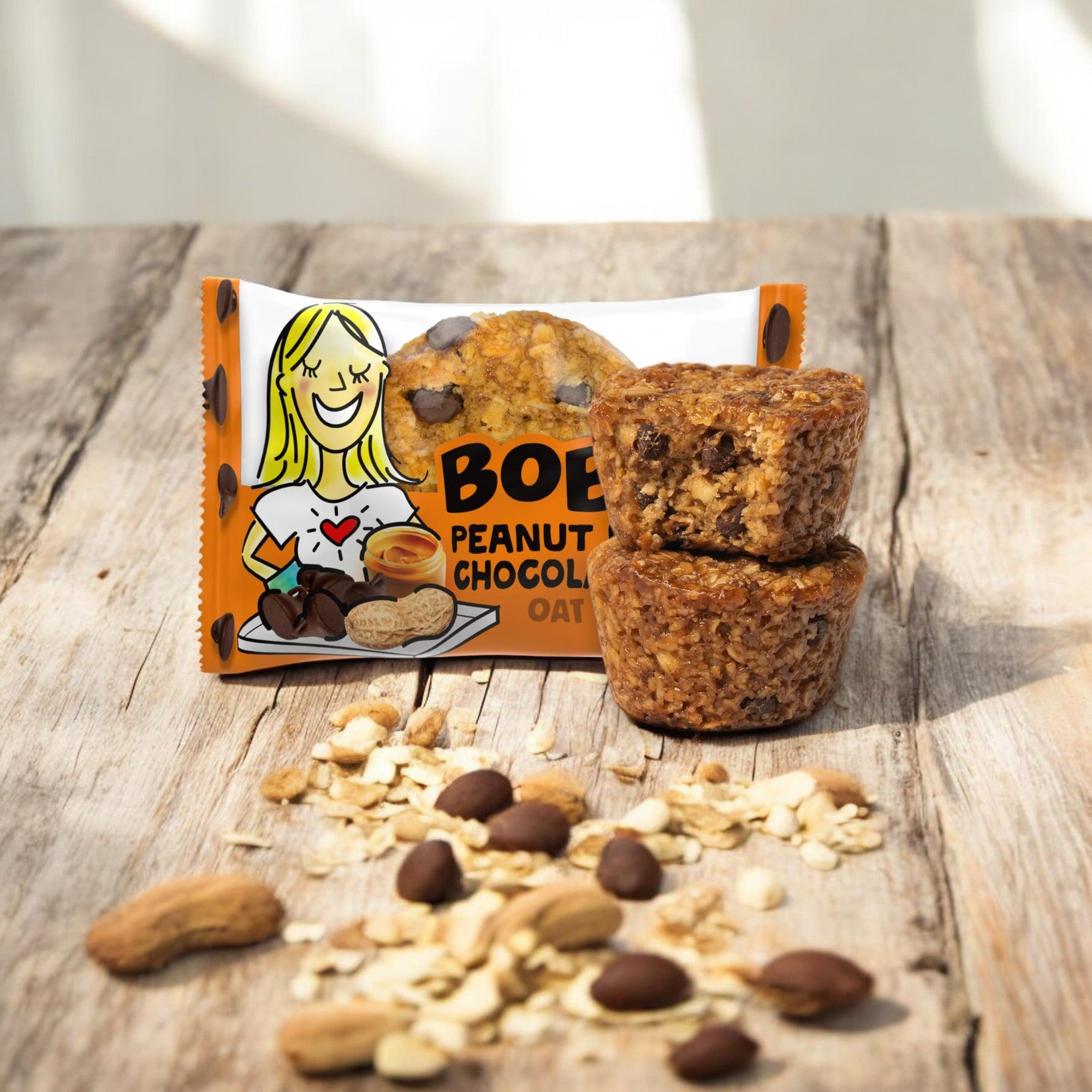 A packet of Bobo's PB & Chocolate Chip Oat Bites, 1.3 oz - 1 Count, made with wholesome ingredients, is displayed with two oat bites stacked beside it and scattered oats, chocolate chips, and peanuts on a wooden surface.