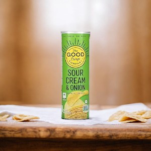 A 5.6 oz can of The Good Crisp Company Sour Cream And Onion potato chips is placed on a wooden table, with a few chips scattered around.