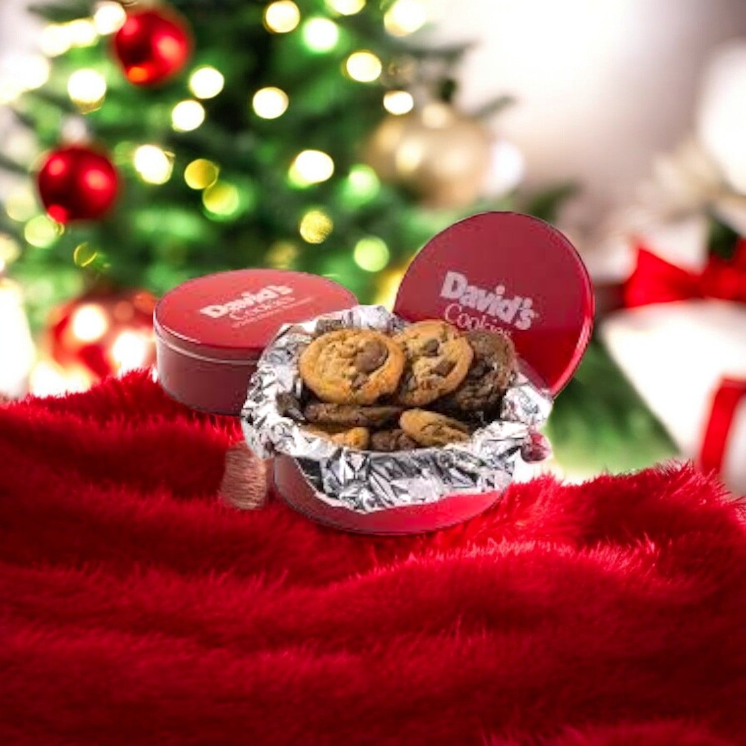 A festive setting with a tin of David's Cookies - Triple Chocolate Cookie Dough on a red blanket in front of a lit Christmas tree, the aroma reminiscent of warm cookie dough filling the air.