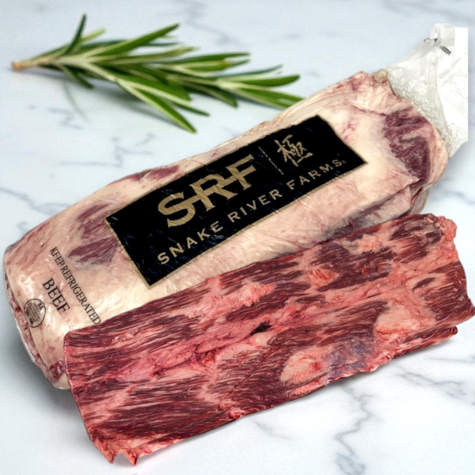Two pieces of raw beef, one packaged with a Restaurant Depot label for Snake River Farms Beef Eye Kalbi – American Kobe Black (6/4 lb avg), are on a white surface with rosemary—ideal for kabobs or diced Halal preparations.