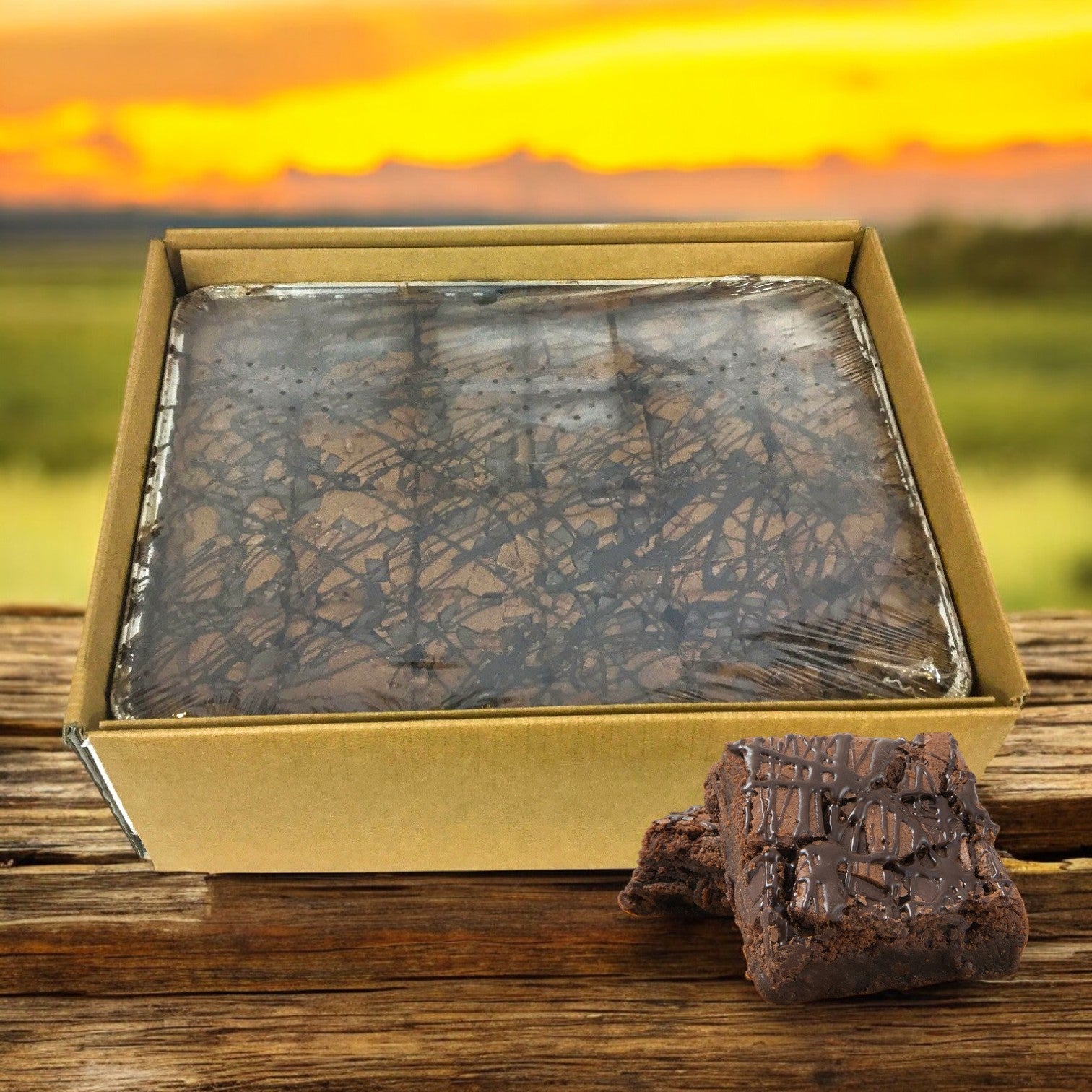 David's Cookies - Double Callebaut Fudge Brownies with a clear lid sit on a wooden surface, framed by a sunset. Two brownies rest outside the box, reminiscent of indulgent chocolate chip cookies.