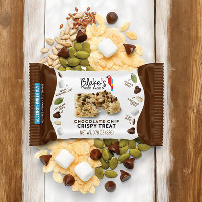 Blake’s Seed Based Crispy Treats — Chocolate Chip -0.78 oz - 1 Count, is showcased against a wooden background. The opened package reveals ingredients such as pumpkin seeds, puffed crisps, and chocolate chips.