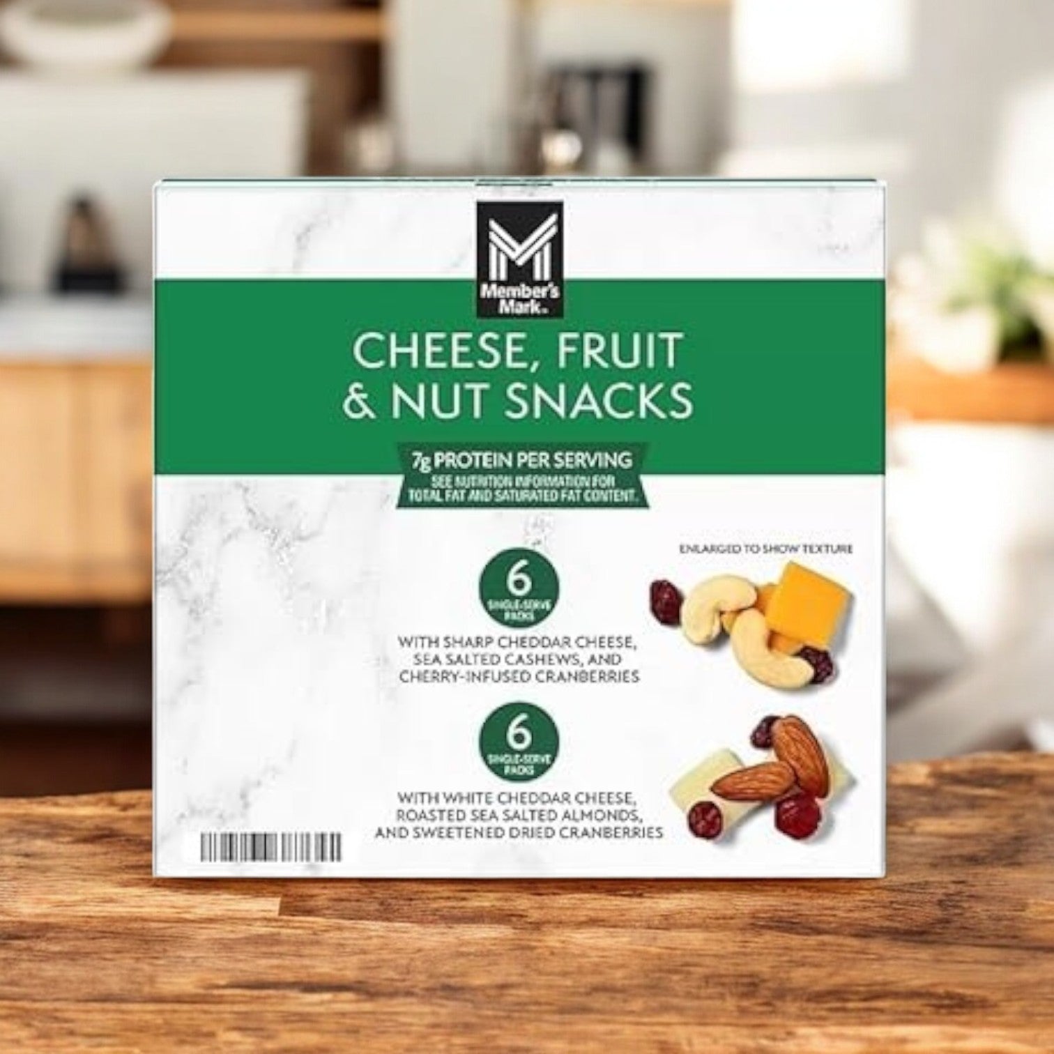 A Member's Mark box of "Cheese, Fruit and Nut Snacks" on a wooden table offers a delicious mix of cheddar cheese, cashews, almonds, and cranberries. The inviting assortment invites enjoyment with an elegant blurred background setting the mood.