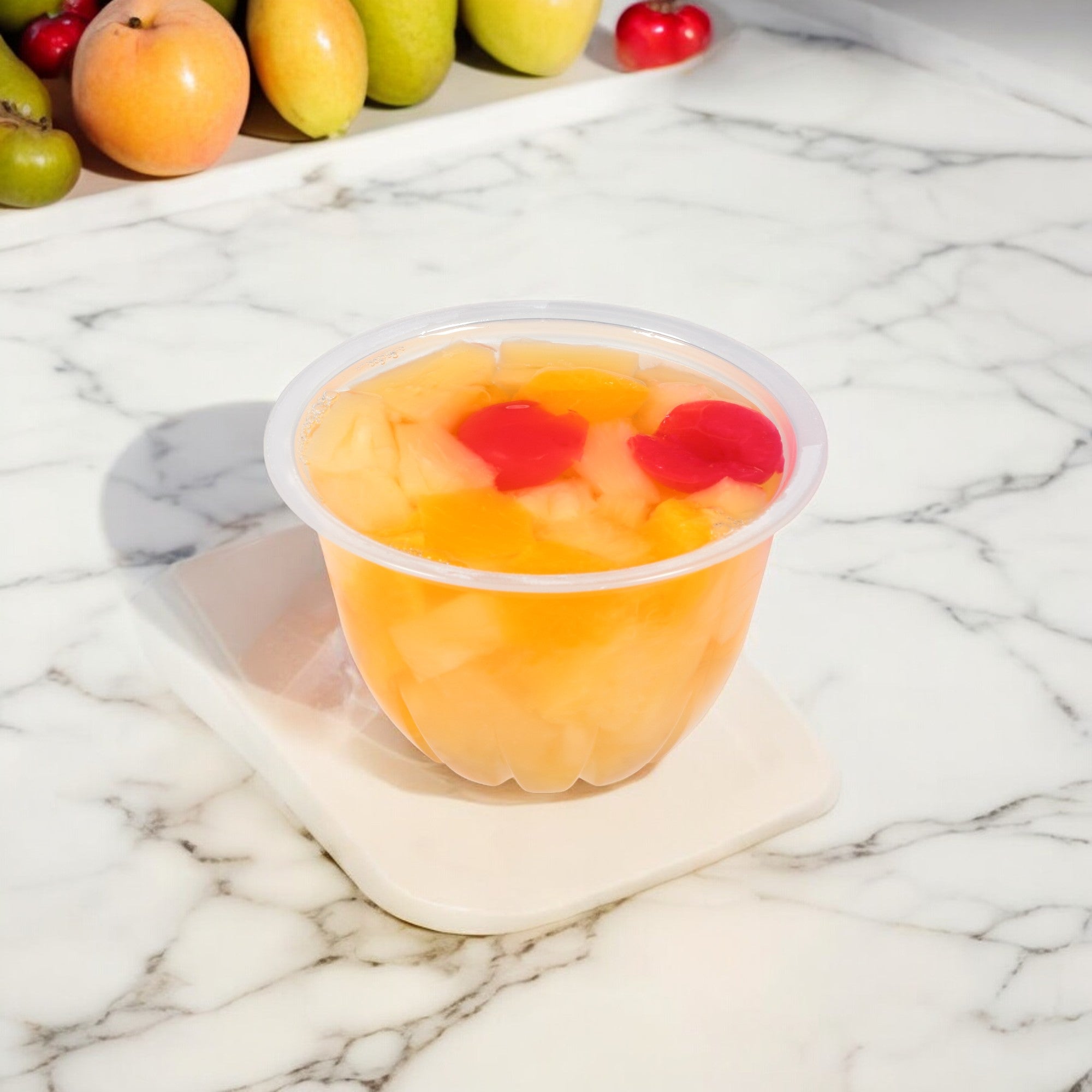 A Dole Fruit Bowls Cherry Mixed Fruit in 100% Fruit Juice, featuring pieces of peaches, pears, and cherries on a white square plate, sits on a marble countertop with various whole fruits in the background. This convenient product from Dole comes in shelf-stable packaging and provides essential Vitamin C for your day.