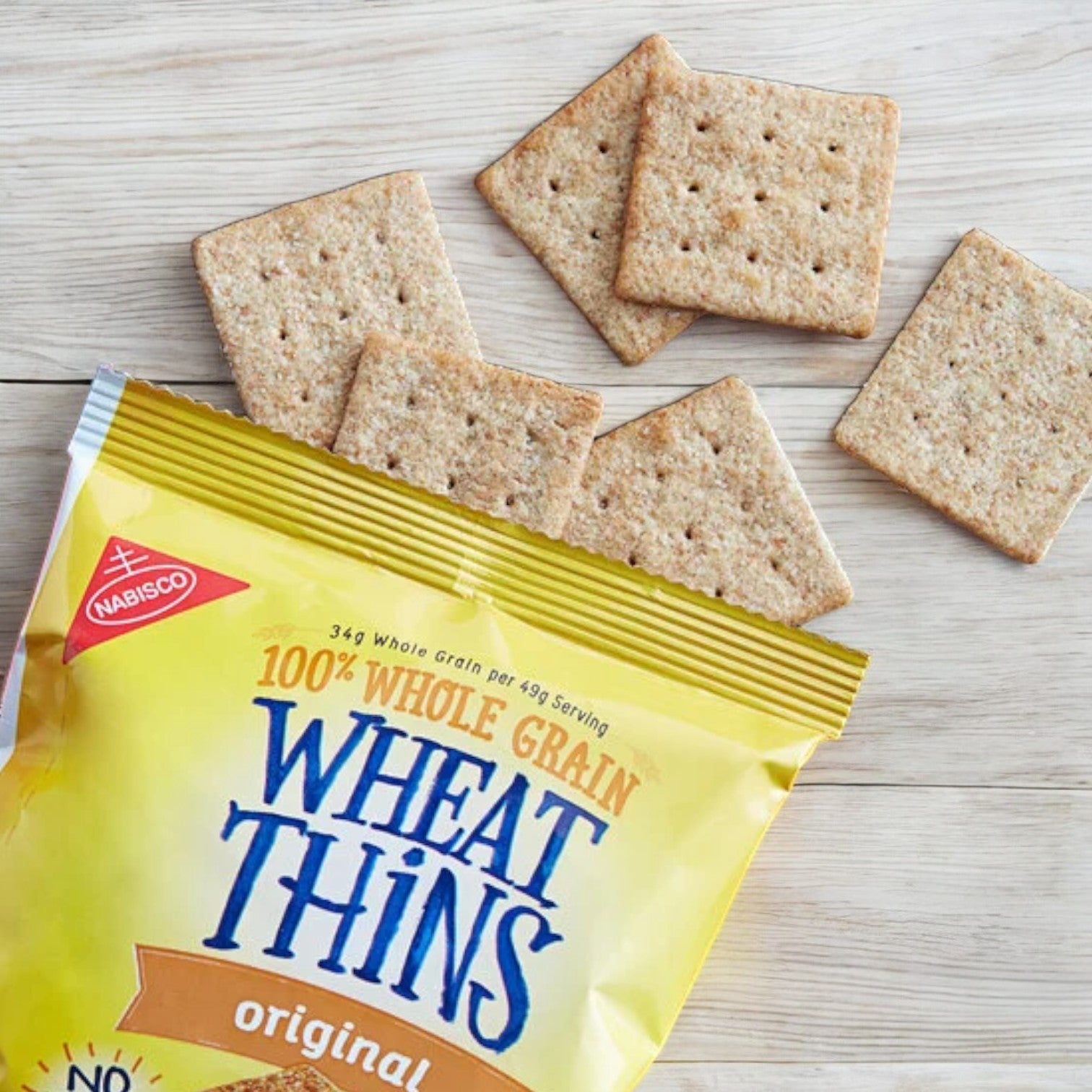 A partially opened package of Wheat Thins 1.75 oz sits on a wooden surface with several whole crackers scattered around it, offering a delightful and healthy snack option.