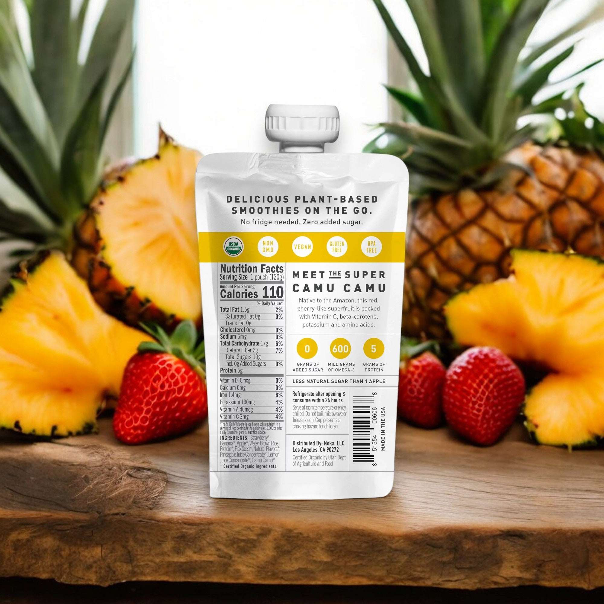 In the foreground, there is a pouch labeled "Noka Organic Strawberry Pineapple Smoothie - 4.22 oz - 1 Count" with nutritional information. Behind it, pineapples and strawberries are arranged on a wooden surface, ideal for an organic superfood smoothie rich in plant protein from Noka.