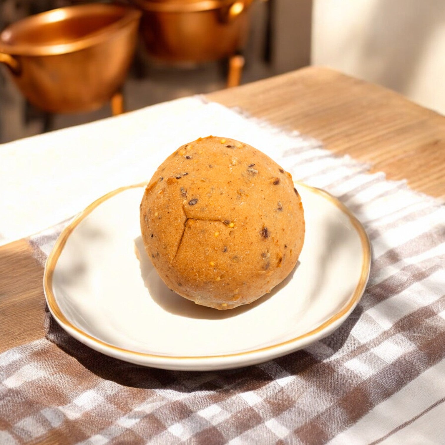 An OMG It's Gluten Free, 5 Grain Dinner Roll, 2 oz. - 1 Count is placed on a white plate atop a checkered cloth on a wooden table, with copper pots in the background.