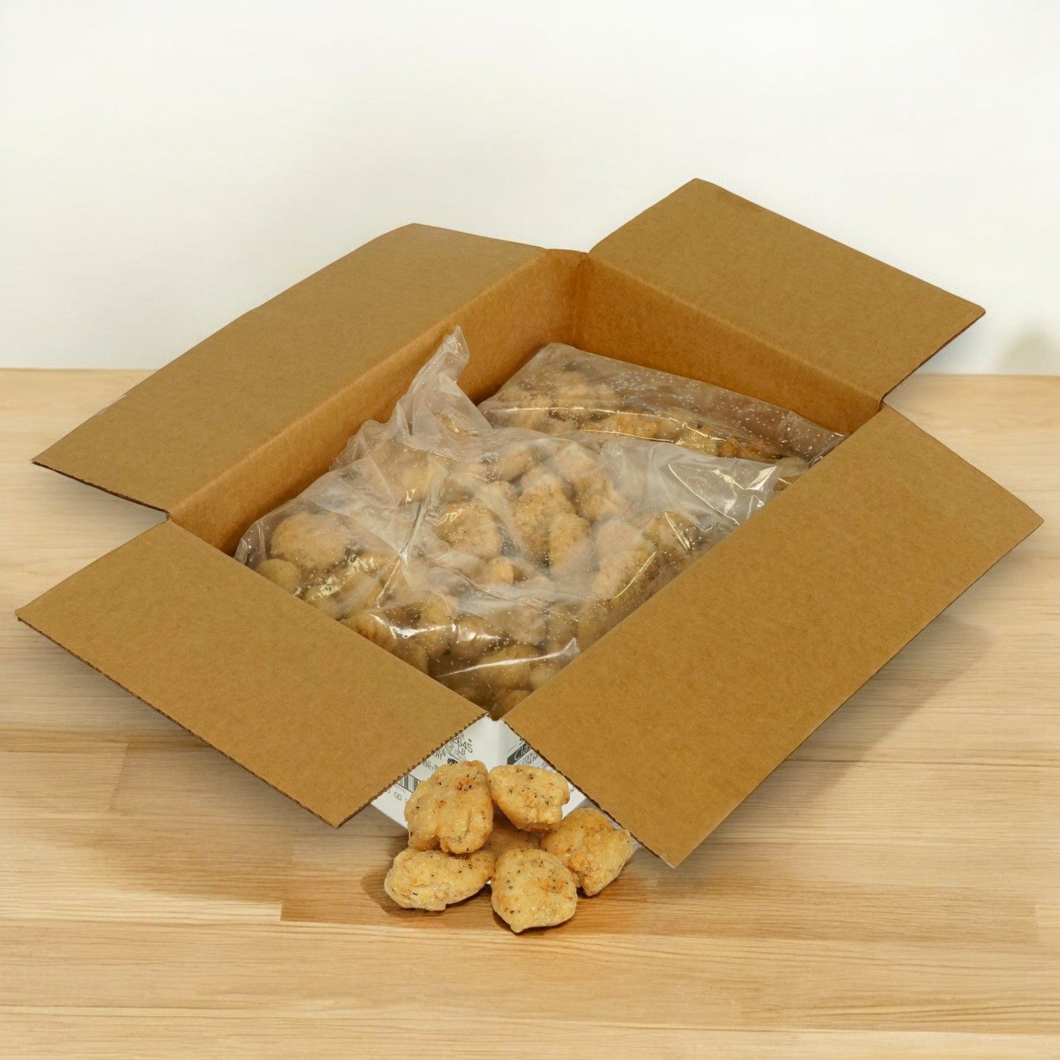 Open a cardboard box containing a large plastic bag of Sysco Classic Chicken Wing Boneless Fully Cooked Gluten-Free Halal - 2/5 lb, with some nuggets spilled on the wooden surface.