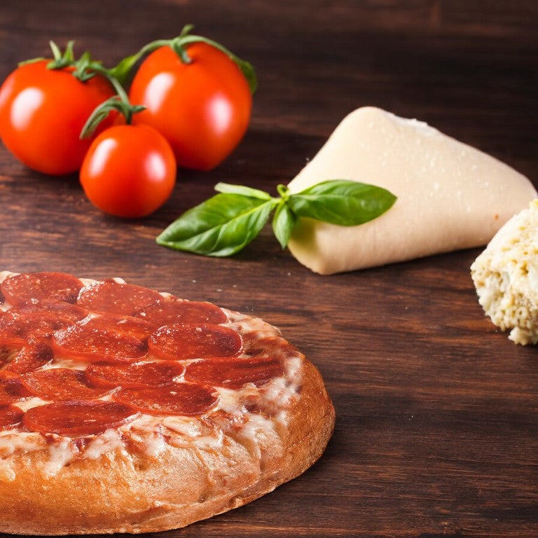 A DiGiorno Original Rising Crust Pepperoni Pizza from a box of three, with melted cheese on a wooden surface, surrounded by fresh tomatoes, basil leaves, a piece of cheese, and a wedge of dough showcases quality ingredients and a perfectly rising crust.