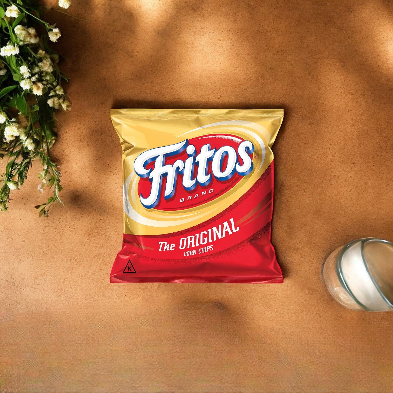 A 1 oz bag of Fritos Original Corn Chips from Frito Lay rests on a tan surface alongside a small bouquet of white flowers and a glass jar, perfect for on-the-go snacking.