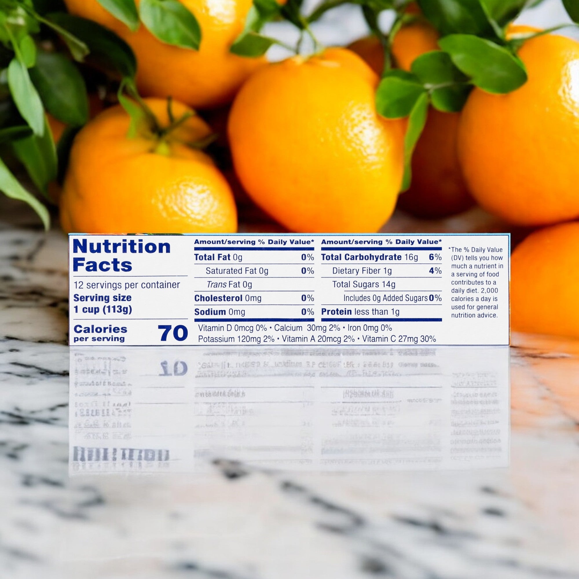 Close-up of a nutrition facts label in front of a cluster of fresh mandarin oranges on a marble surface. The label highlights detailed nutritional information per 1 cup (113g) serving, including 70 calories. Perfect for creating non-GMO fruit cup snacks with Del Monte Mandarin Oranges Fruit Cups, No Sugar Added.