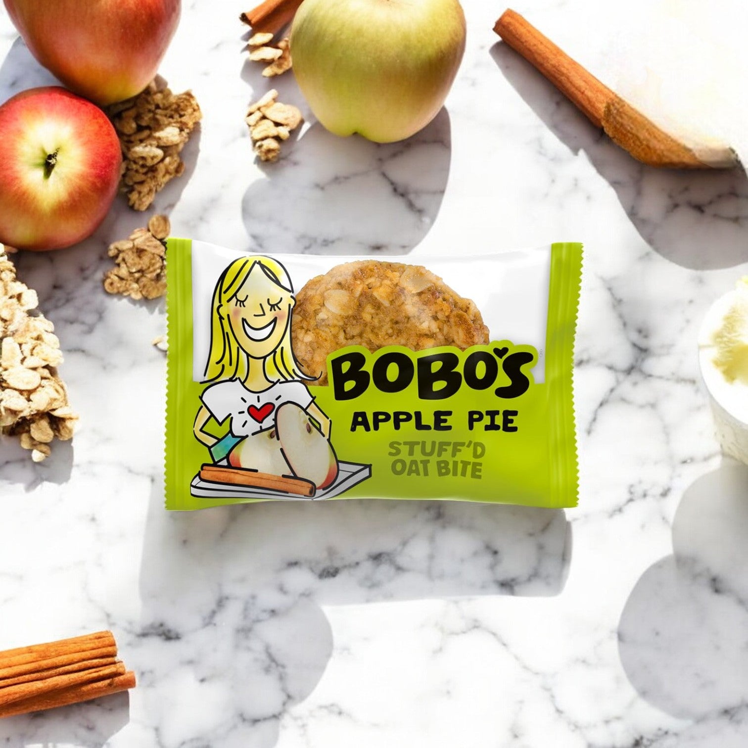 A package of Bobo's Stuff'd Apple Pie Bites - 1.3 oz - 1 Count, made with wholesome whole grain oats, is placed on a marble surface, surrounded by apples, oats, cinnamon sticks, and apple slices.