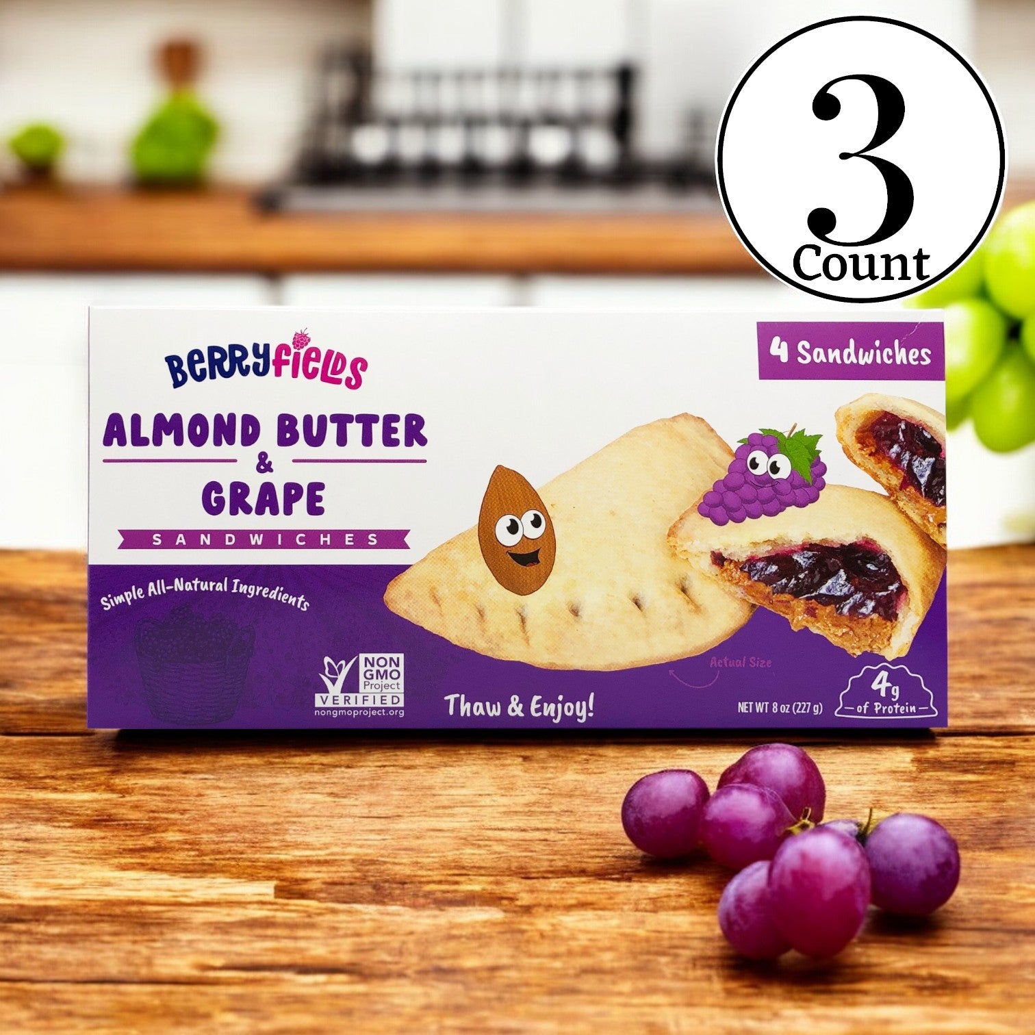 Berryfields Almond Butter & Grape Sandwiches, 8 oz. -3 Count, known for being gluten-free, are presented on a wooden surface with grapes in the foreground. The packaging displays images of the sandwich and features purple accents, emphasizing the rich flavors inside.