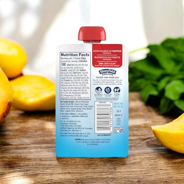 Back view of a Stonyfield's Organic Pear Spinach Mango Kids' Yogurt pouch with visible nutrition facts and ingredients list, surrounded by cut peaches and fresh spinach on a wooden surface—perfect for a kid-friendly snack.