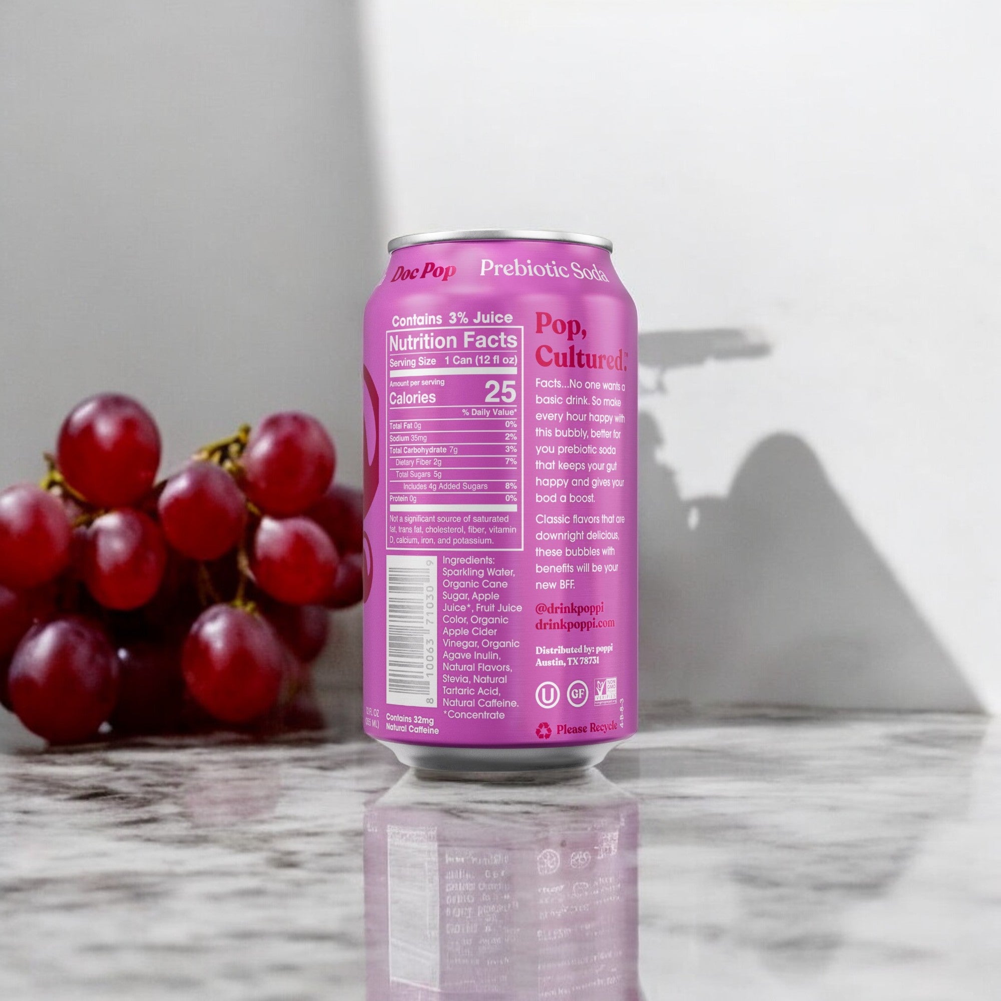 A can of Poppi: Doc Pop Prebiotic Soda stands on a marble surface. Nutrition facts are visible on the can. A bunch of red grapes is in the background, highlighting this low-calorie beverage from Poppi as a healthy alternative.