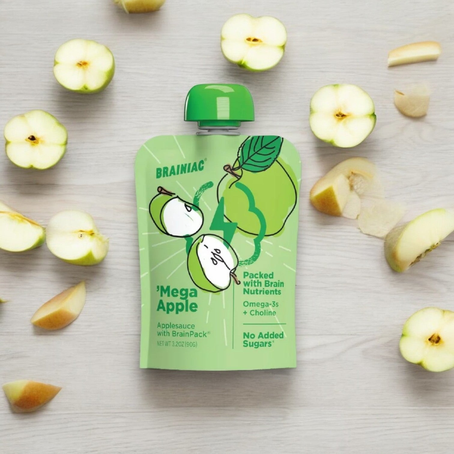 A green applesauce pouch labeled "Brainiac Brain Squeezers Applesauce with Omega-3s, Apple, No Sugar Added" by Brainiac lies on a light wooden surface surrounded by sliced apples. The packaging highlights brain nutrients, Omega-3s, choline, and no added sugars, making it a nutritious snack for all ages.