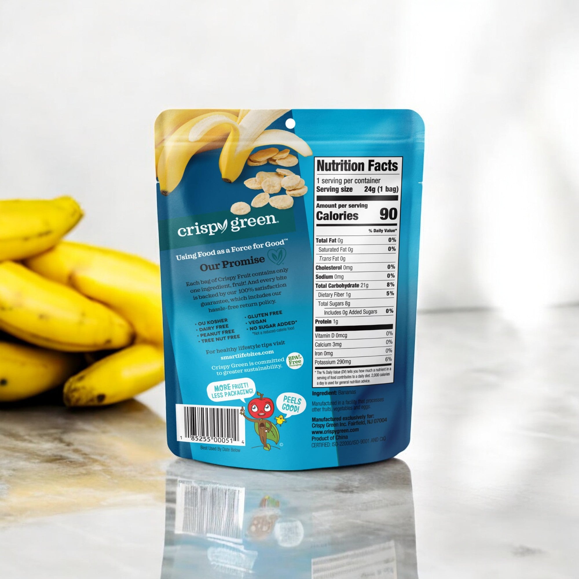 A bag of Crispy Green Crispy Fruit All Banana - 0.35 oz is displayed on a marble countertop, with fresh bananas in the background. The nutrition facts and ingredients are visible on the back of the bag, highlighting Crispy Green’s commitment to sustainability and authentic taste.