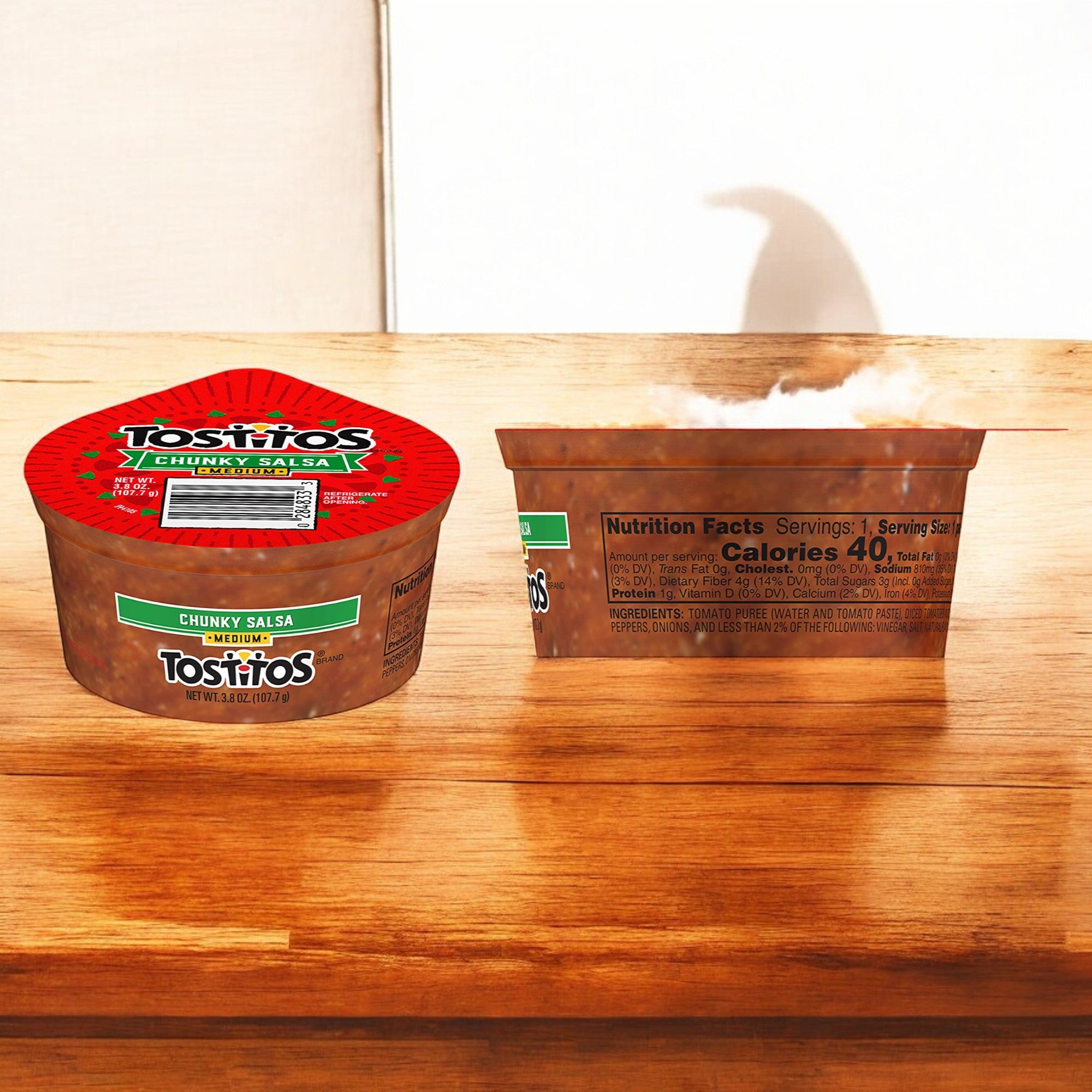 A container of Tostitos Medium Chunky Salsa Dip - 3.8 oz sits on a wooden surface, with one closed and another open to reveal the delicious contents inside. Perfect as a portable snack or for single-serving salsa portions at your next gathering.