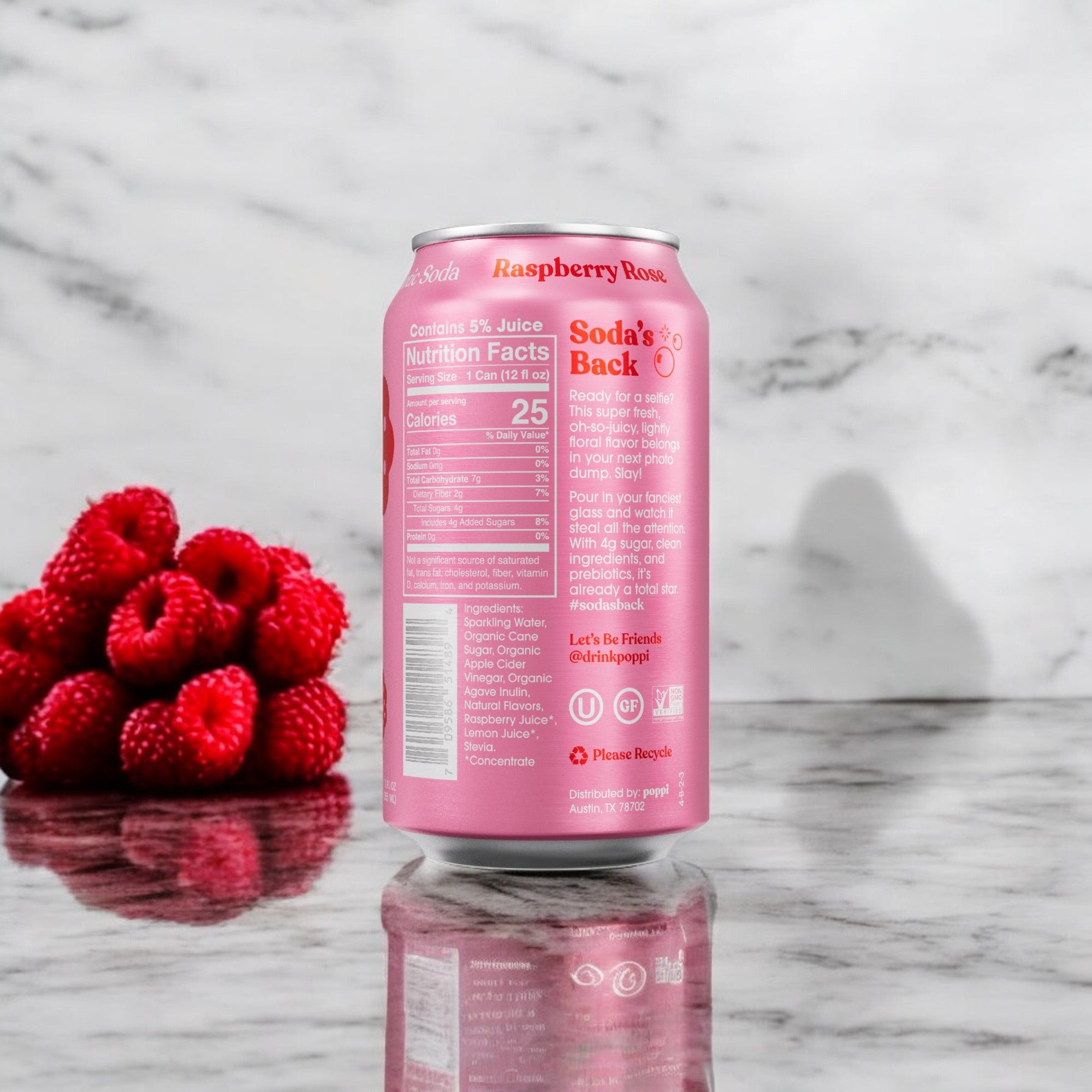 A can of Poppi Prebiotic Soda in the Raspberry Rose flavor, with its distinctive pink design, rests on a marble surface next to a small pile of fresh raspberries. The back label of the 12 fl oz can is visible, showcasing it as a low-calorie beverage enriched with prebiotics.