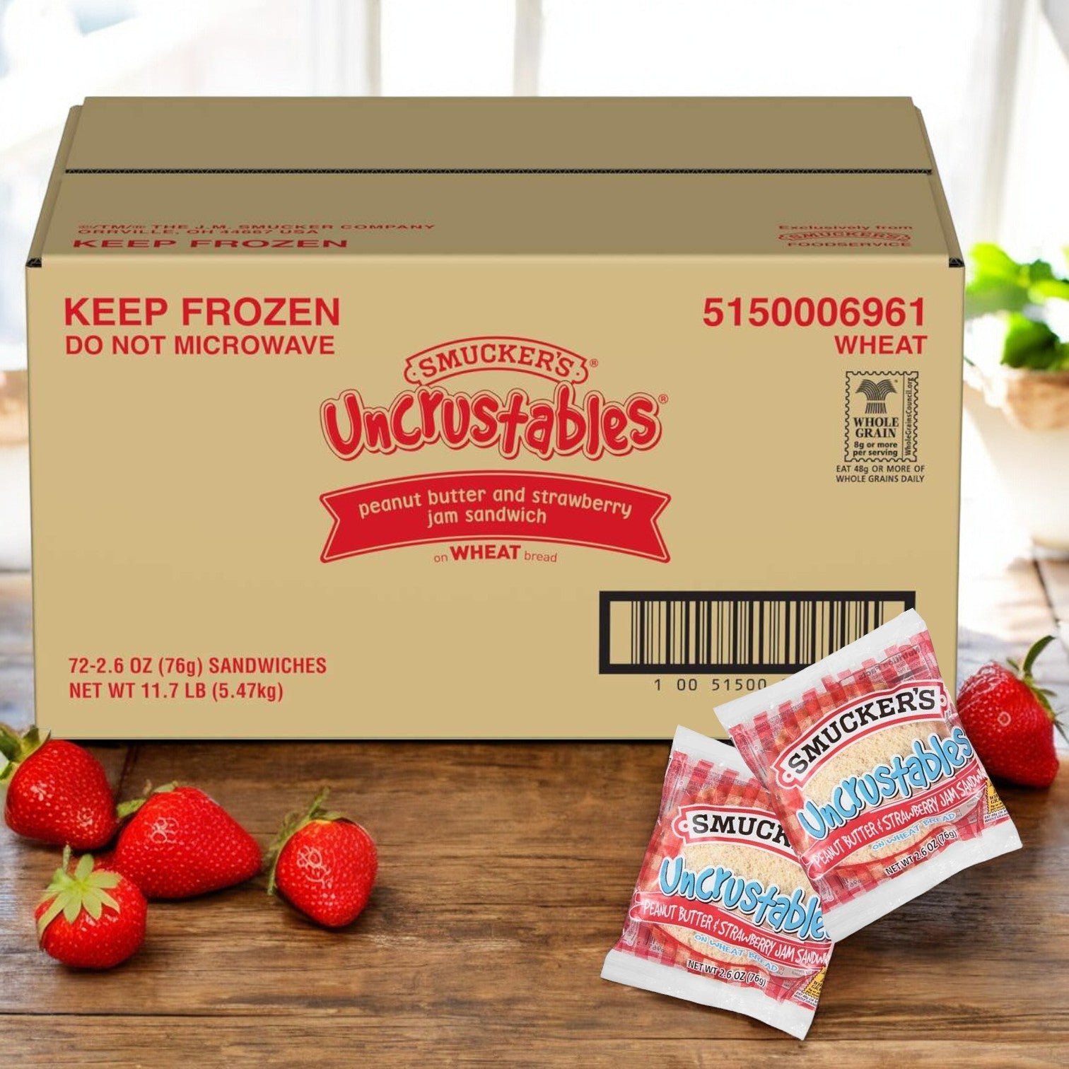 A box of Uncrustable Smuckers' Uncrustables Strawberry Jam - Bulk 72 Count, featuring a harmonious blend of flavors in two handheld snacks, with fresh strawberries placed in front.