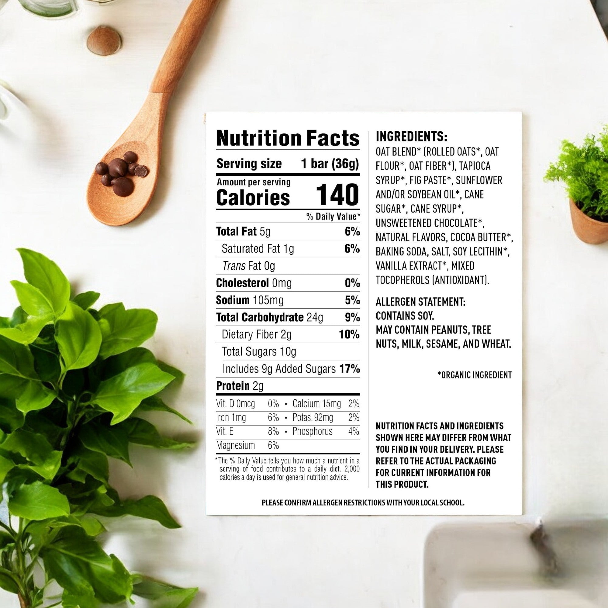 A nutrition facts label and ingredients list for Clif Bar Z Bar Chocolate Chip Z Bar Cliff Kid -1.27 oz-1 Count, placed on a white surface near a wooden spoon with coffee beans and fresh green herbs. Perfect for on-the-go snacking, the label provides calorie and nutrient information, highlighting the benefits of whole grains.