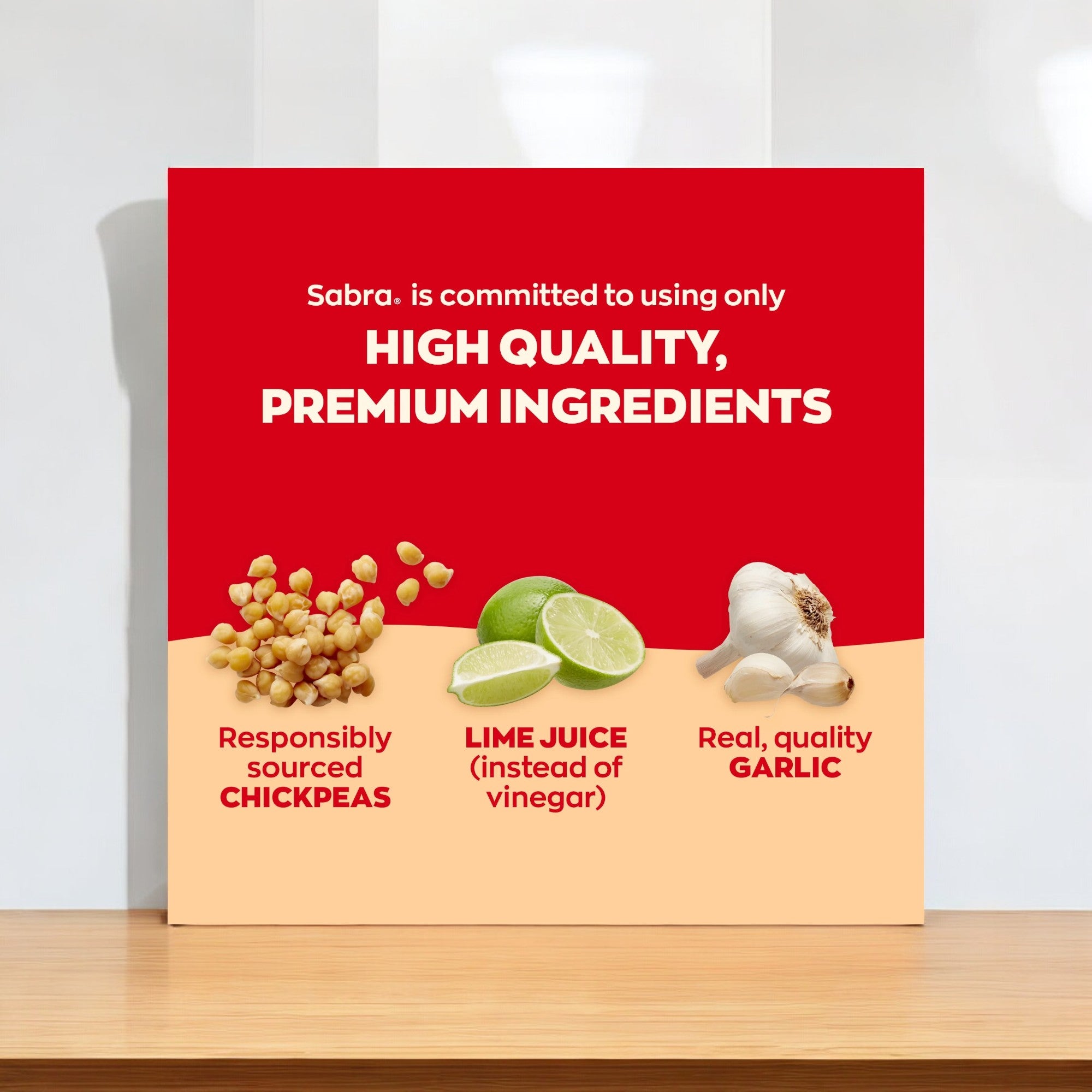 Promotional sign spotlighting Sabra's dedication to premium ingredients, showcasing ethically sourced chickpeas, lime juice in place of vinegar, and genuine, high-quality garlic. Relish in Sabra Classic Hummus Singles—a delectable plant-based snack offered in handy 2 oz plastic cups (6 Pack).