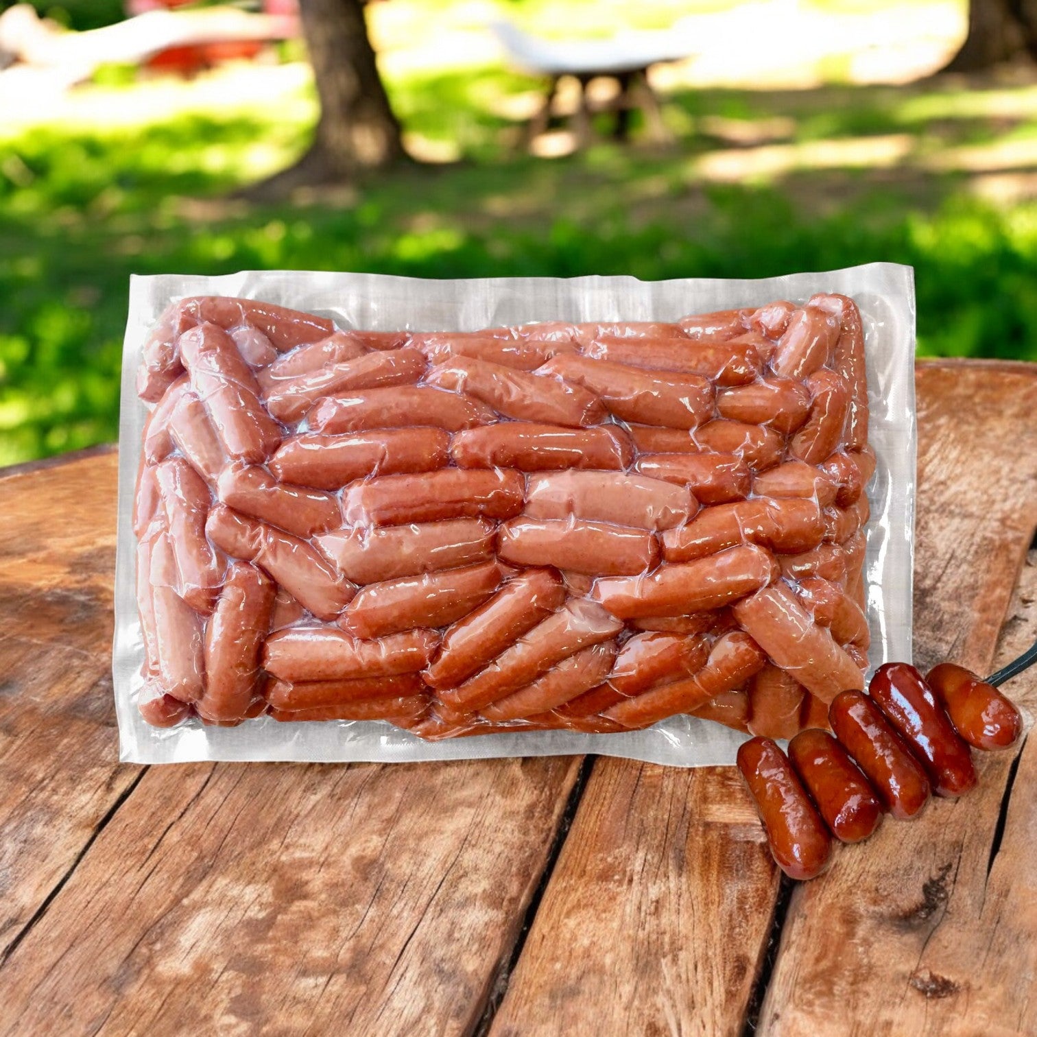 A vacuum-sealed package of Vienna Beef Cocktail Franks- 3 Count is displayed on a wooden table outdoors, with a skewer of four cooked Vienna Beef franks resting beside it.