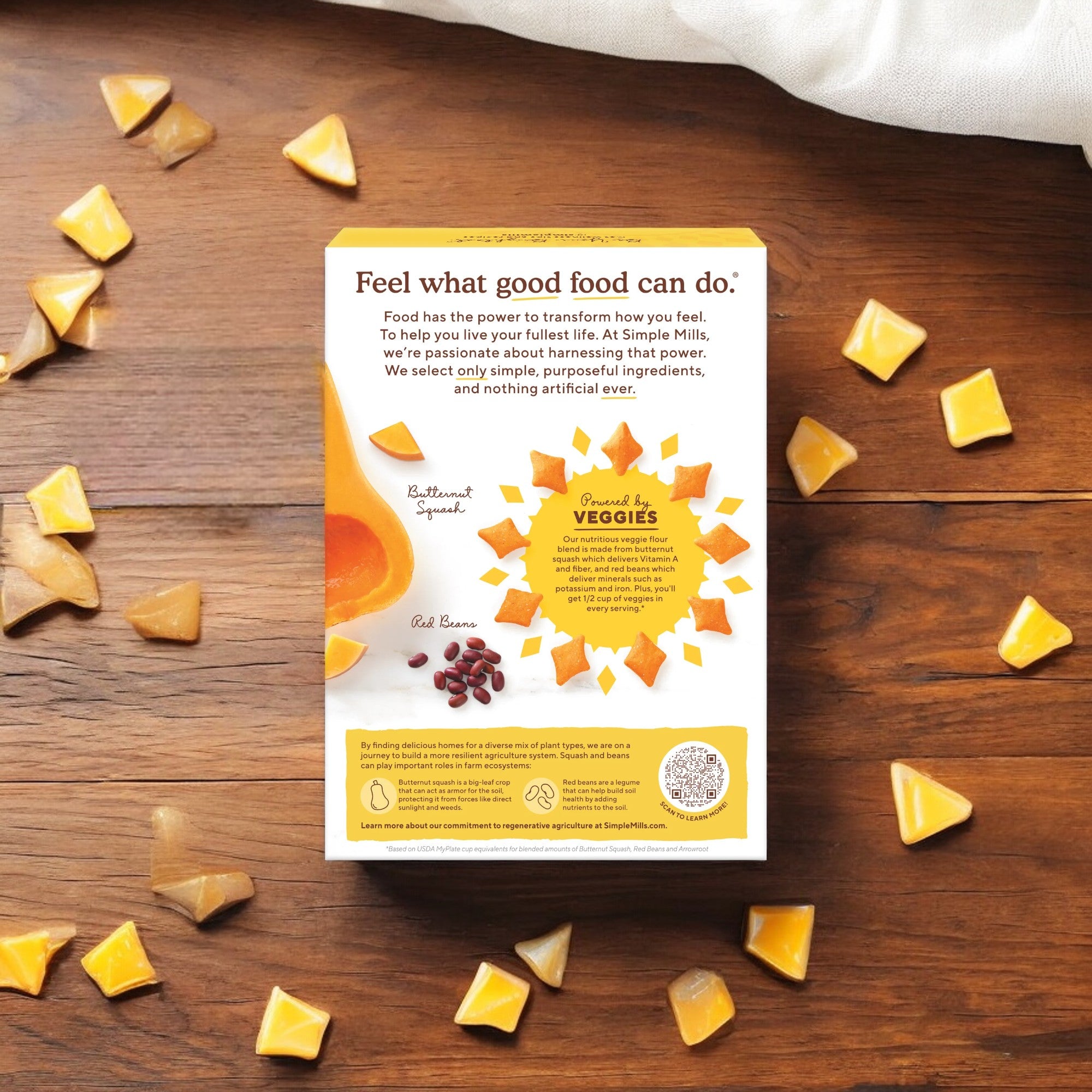 A food package from Simple Mills reads "Feel what good food can do." It underscores the use of purposeful ingredients with minimal artificial additives, showcasing Simple Mills Cheddar Pop Mmms, Gluten Free Baked Snack Crackers (4 oz) surrounded by small triangular yellow snacks on a wooden surface.