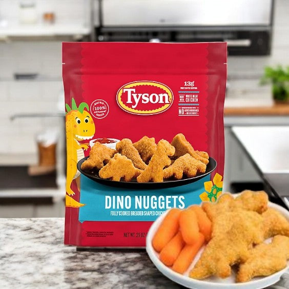 A Tyson Dino Nuggets package is on the kitchen counter, highlighting their whole-grain appeal. In front, a plate of these fully cooked dinosaur-shaped chicken nuggets pairs perfectly with crisp carrot sticks.