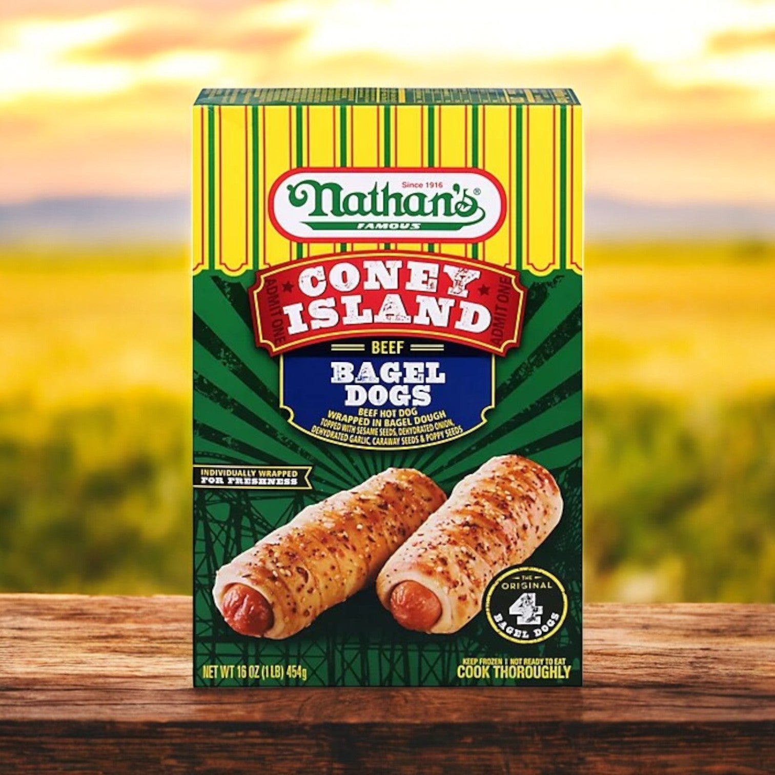 A 20 oz Nathan’s Famous Coney Island Bagel Dogs box sits on wood with a field backdrop. The package shows two enticing bagel dogs and proclaims the contents—four beef bagel dogs ready to savor.