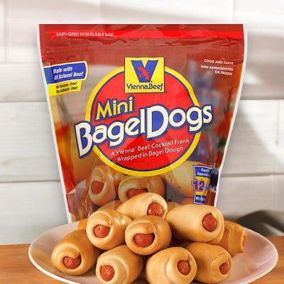 A plate of Vienna Beef Natural Mini Bagel Dogs sits in front of a resealable bag labeled "Vienna Beef Natural Mini Bagel Dogs." Made with all-natural beef, these cocktail franks wrapped in bagel dough offer a delicious and convenient snack option.