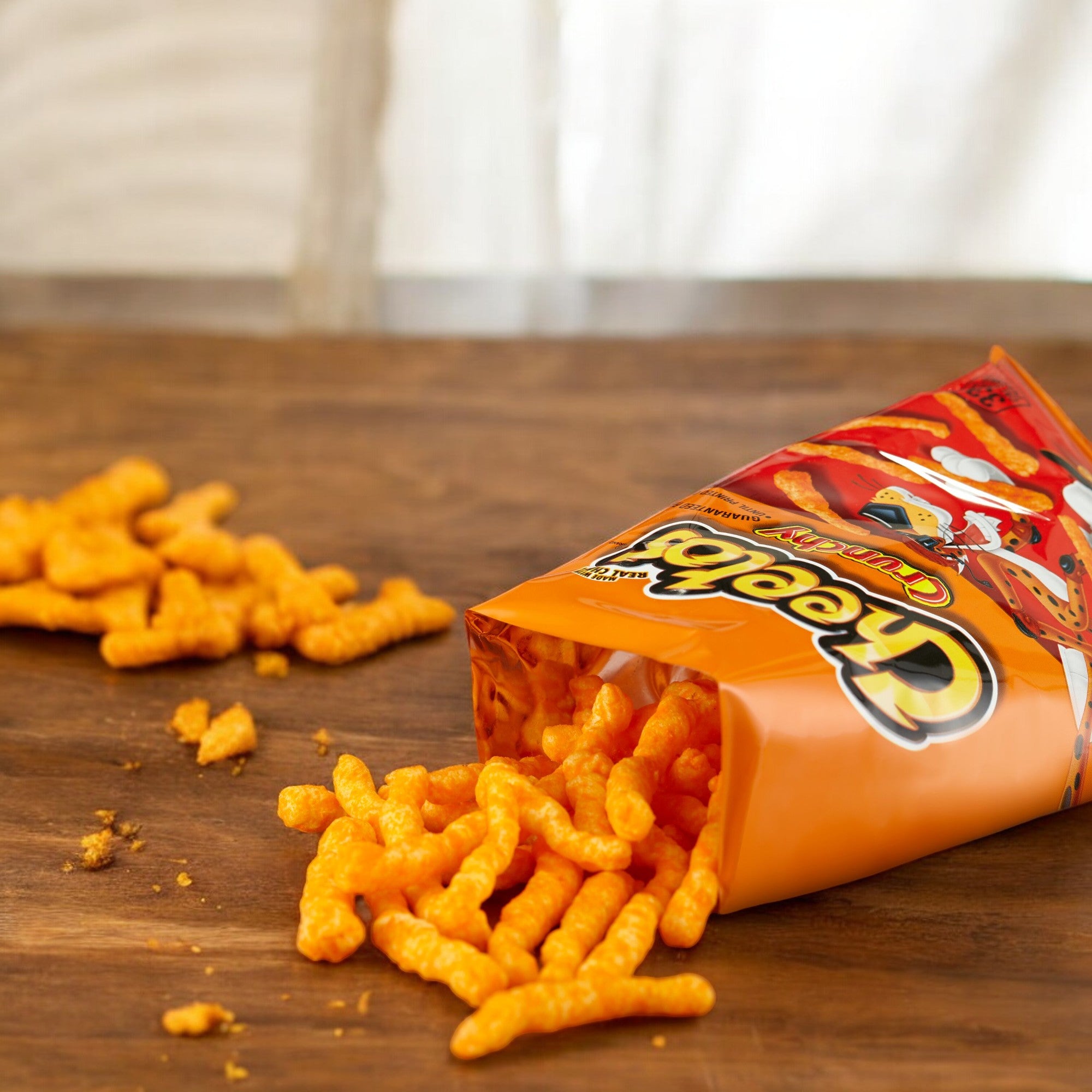 An open 1 oz bag of PepsiCo's Cheetos Cheese Chips lies on a wooden surface, with some of the real cheese treats spilling out.