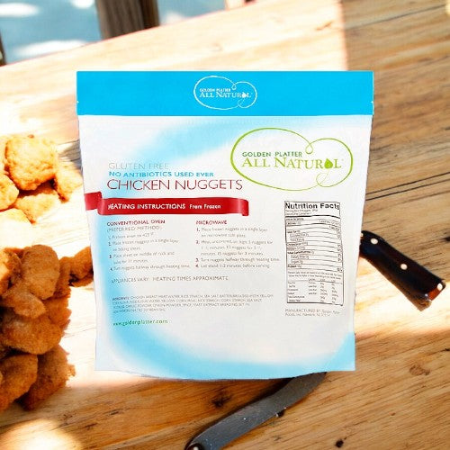 A package of Golden Platter Gluten Free Nuggets, 4 lbs is displayed on a table next to a pile of cooked, breaded chicken nuggets and a knife. Featuring chicken breast and made with non-hydrogenated soybean oil, the package details nutritional and cooking information.