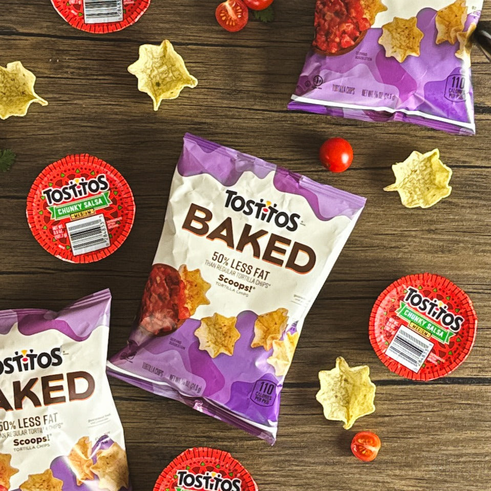 Bags of Tostitos Baked Scoop with Tostitos Chunky Salsa and containers of Chunky Mild Salsa are arranged on a wooden surface, surrounded by scattered chips and a red bell pepper, creating the perfect snacking experience.