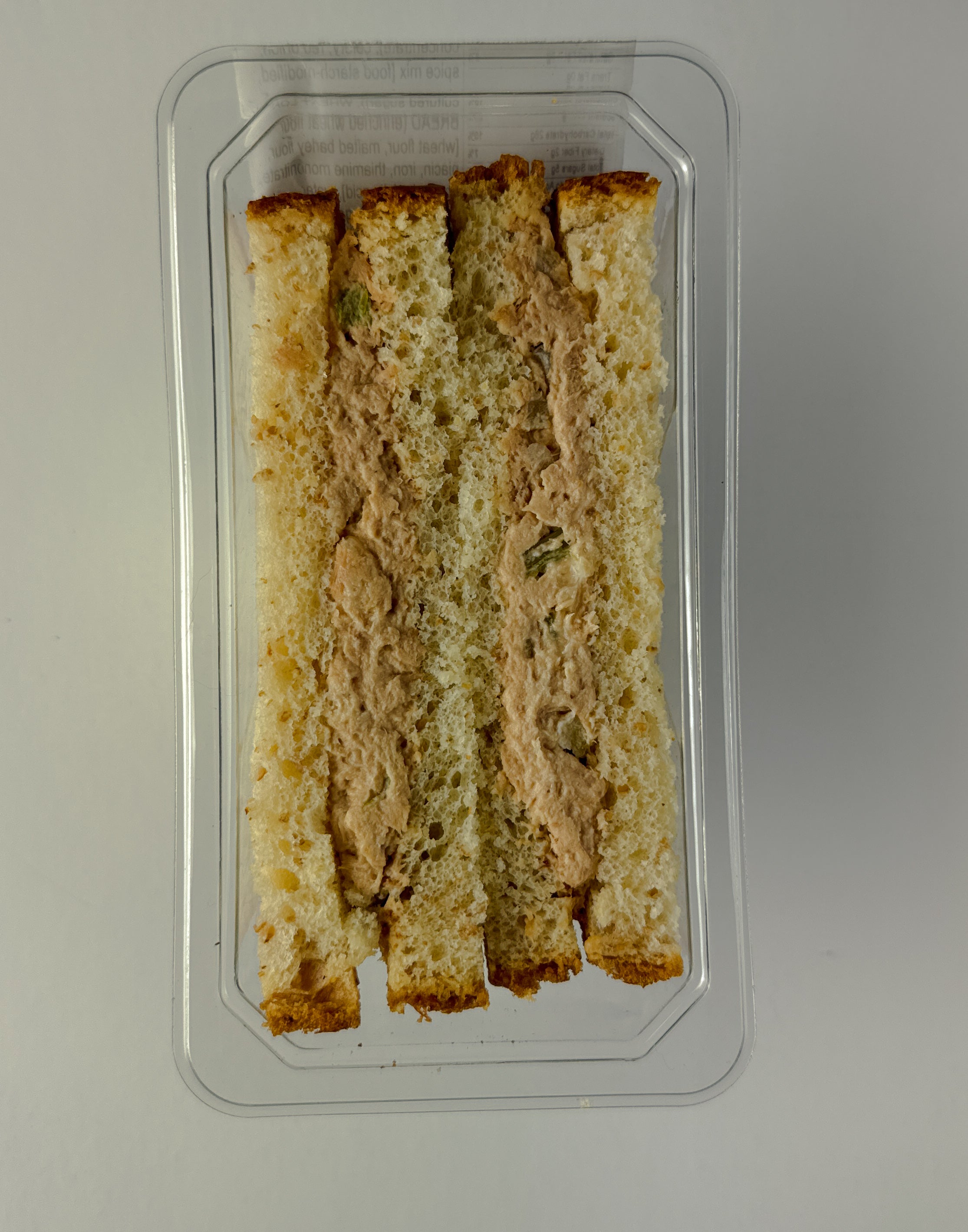 A clear plastic container from Taylor Farms holds four rectangular strips of lightly toasted bread, visibly filled with a delicious tuna salad made with canola mayonnaise. The product is aptly named the Tuna Salad Sandwich.