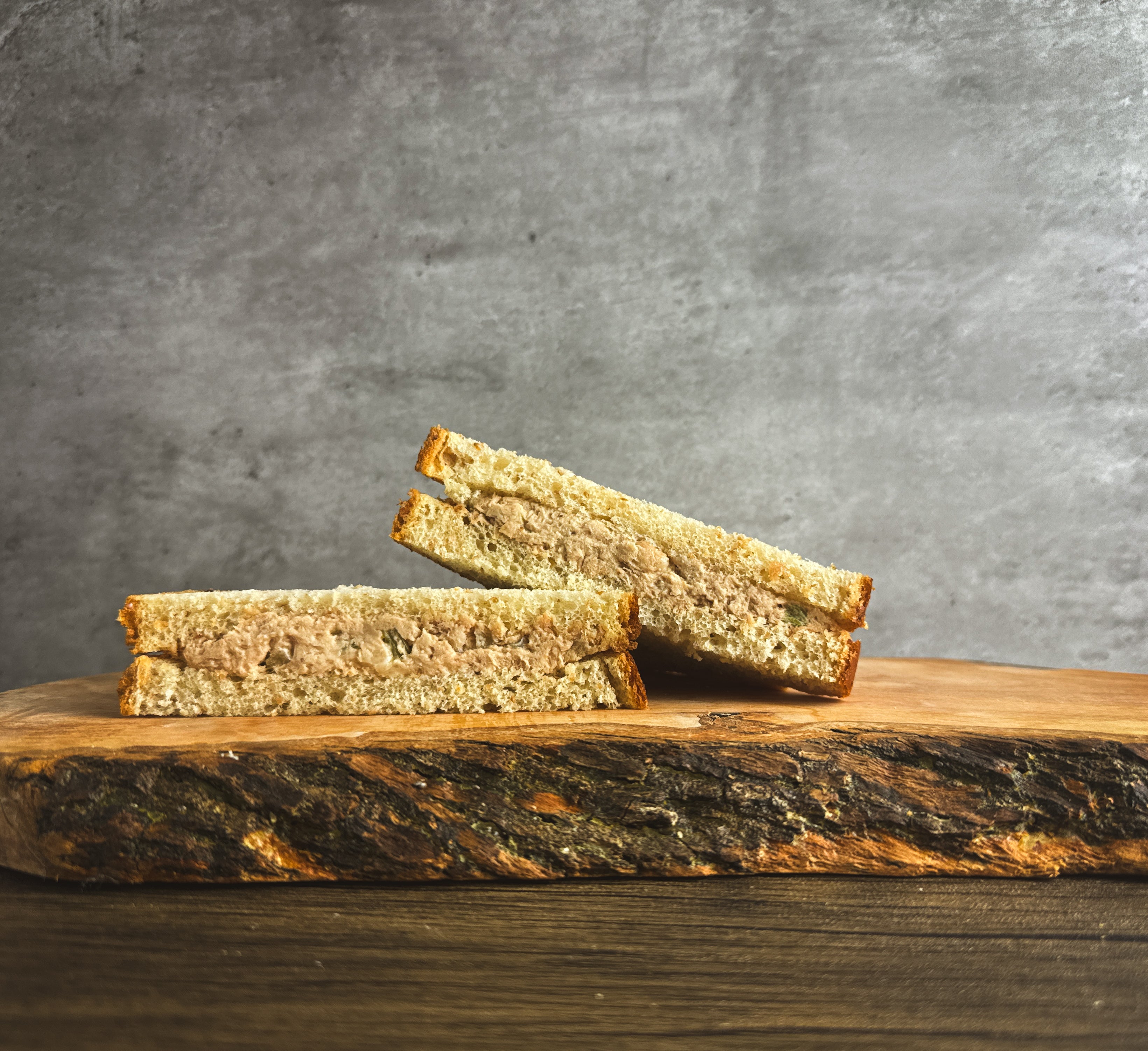 A Taylor Farms Tuna Salad Sandwich arranged on a wooden cutting board against a gray textured background.