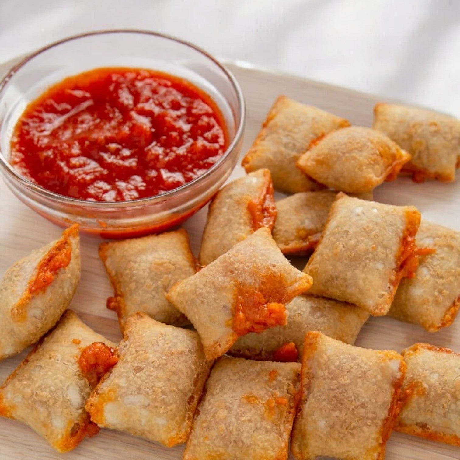 A plate of rectangular pizza bites featuring classic pizza flavors is arranged next to a bowl of marinara sauce, reminiscent of Totino's Pepperoni Flavored Pizza Rolls, 24.8 oz frozen snacks.