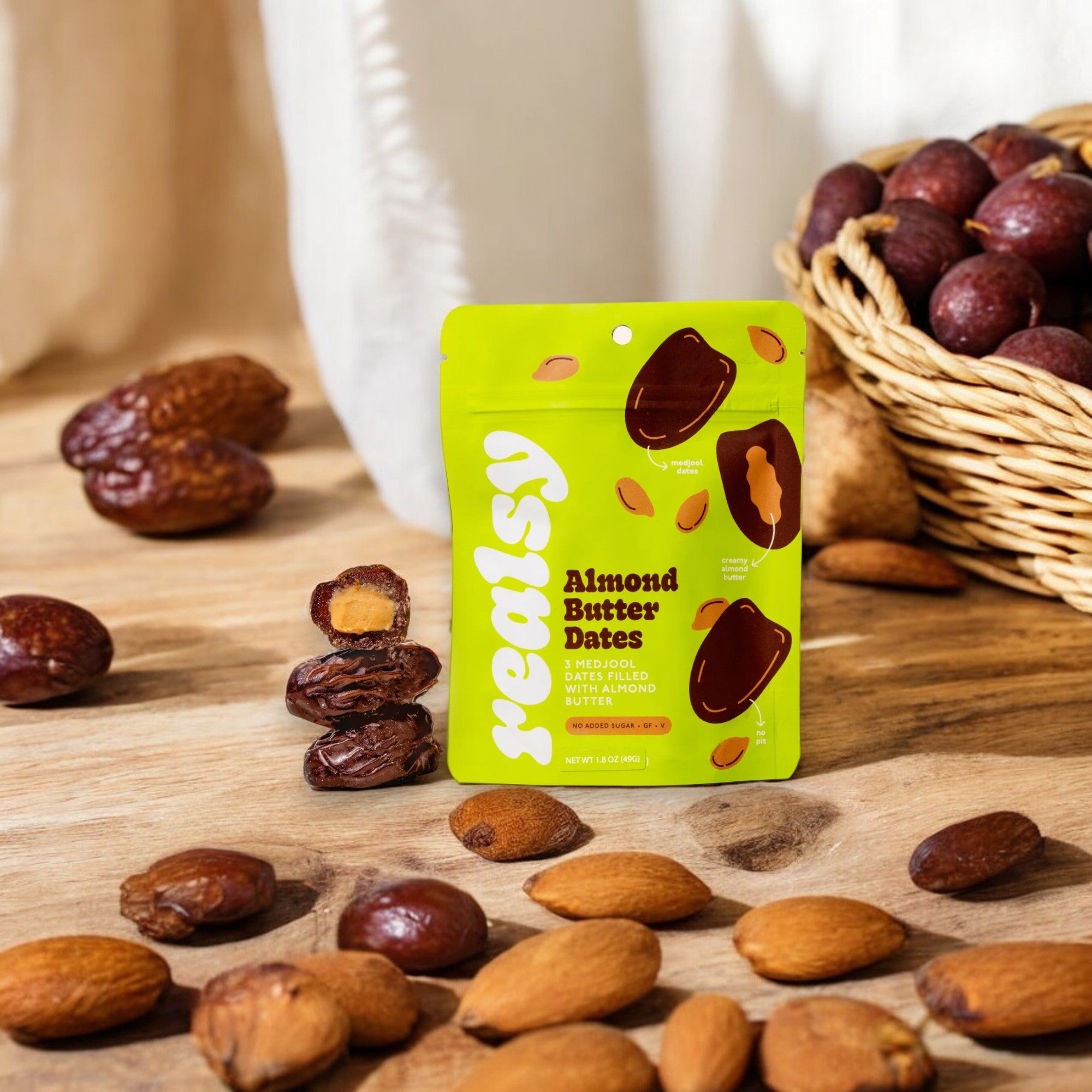 A package of Realsy Almond Butter Dates by Realsy is displayed among dates and almonds on a wooden table, emphasizing the naturally sweet produce from a family-owned date farm. In the background, a basket of dates adds to the rustic and wholesome scene.