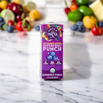 An Uncle Matt's Superfruit Punch Juice Box, 6.75 oz - 1 Count is placed on a marble surface, embodying the perfect choice for convenient portable drinks, with various fruits blurred in the background.