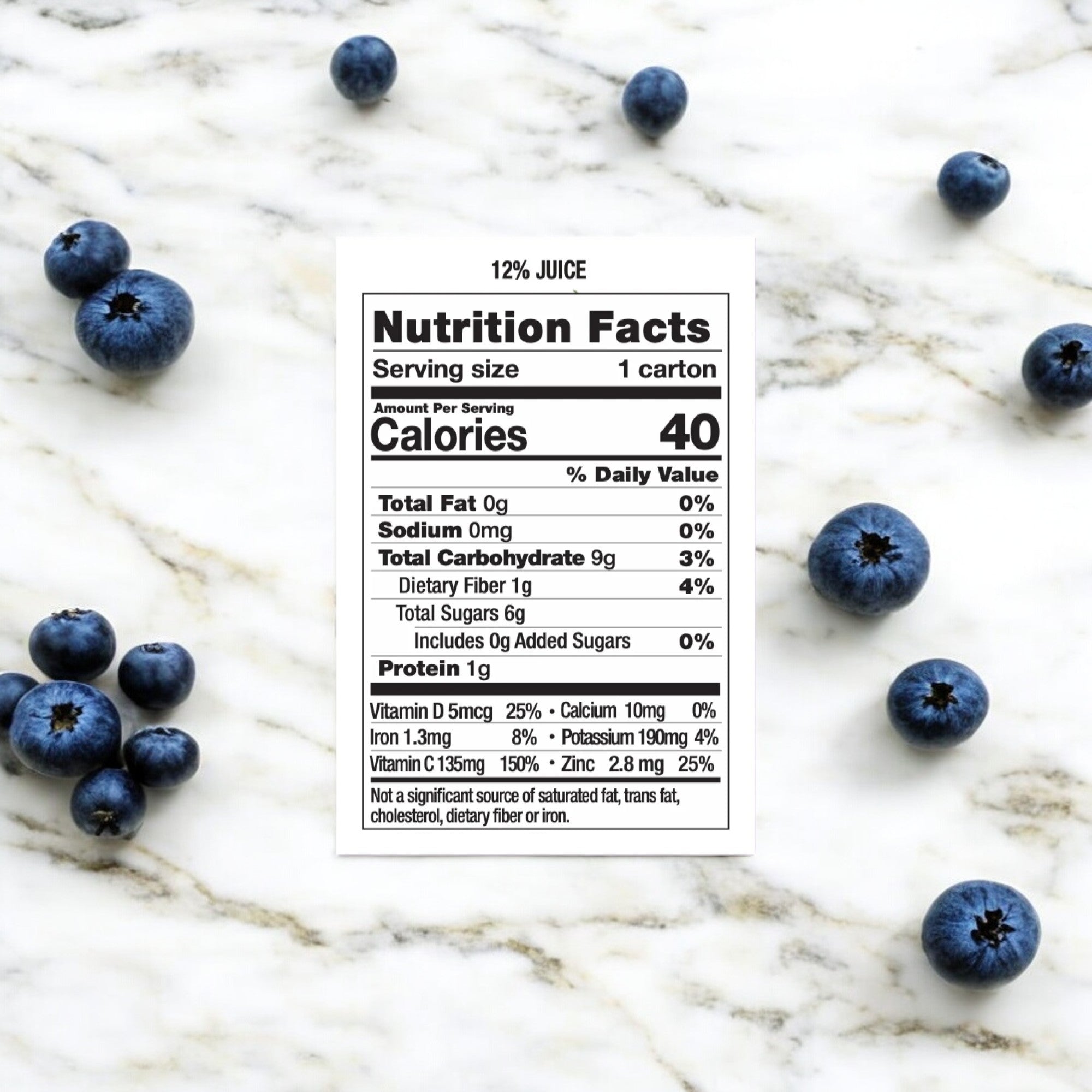 A nutrition facts label for Uncle Matt's Superfruit Punch Juice Box, 6.75 oz—featuring 12% organic juice and 40 calories per serving—placed on a marble surface with scattered blueberries around it.