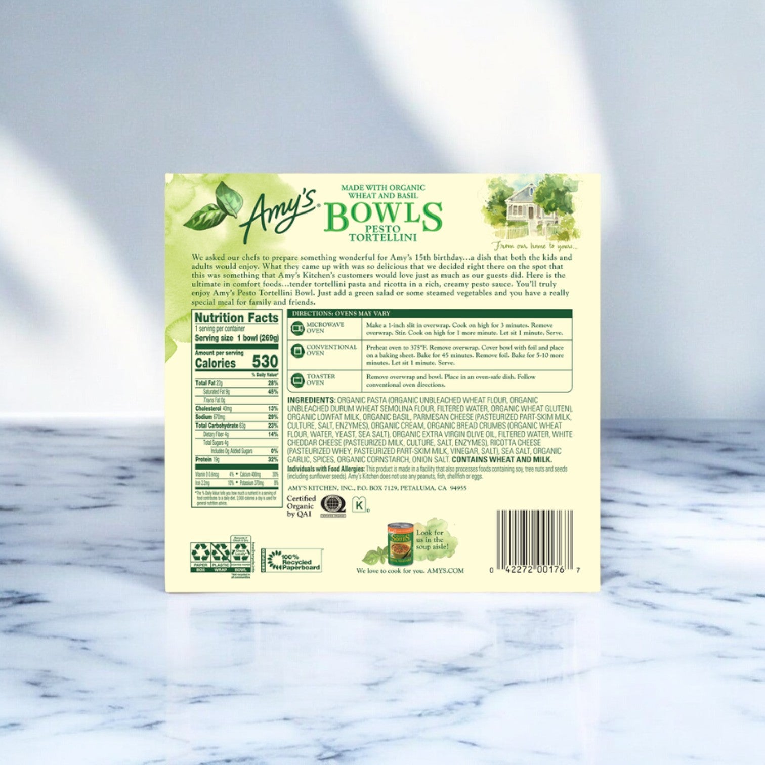 The back of a box of Amy's Kitchen Bowls Pesto Tortellini, 9.5 oz., displays nutritional facts, ingredients, certifications, and preparation instructions against a light marble surface. Enjoy this organic Italian-inspired meal with ease and confidence.