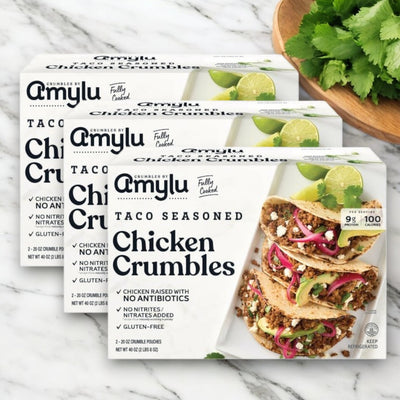 Amylu Taco Seasoned Chicken Crumbles, 40 oz. - 3 Packs, are displayed with tacos filled with fully cooked chicken and cilantro on a marble surface—ideal for quick and easy meal prep.