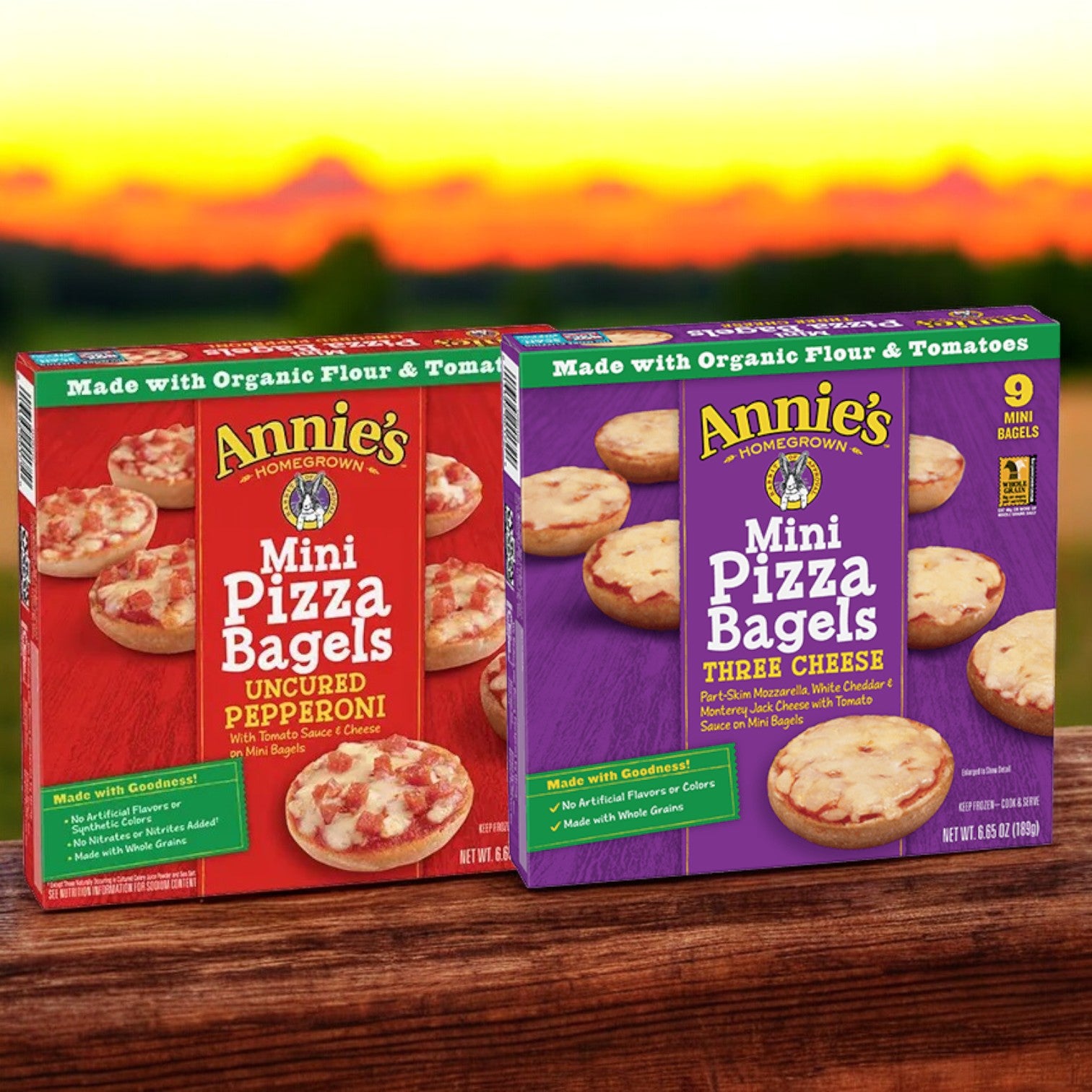 Against a sunset backdrop, the Annie's Mini Pizza Variety Packs are displayed, featuring one box of Uncured Pepperoni Mini Pizza Bagels and one box of Three Cheese Mini Pizza Bagels for a total of two packs.