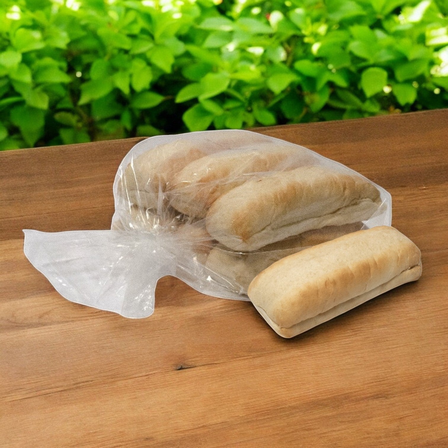 A plastic bag of Easy Lunches Italian Beef Hoagie Buns - 6 Pack Hoagie Hearth Hinged 6" Buns, with one bun partially removed, sits on a wooden table. Greenery is visible in the background.