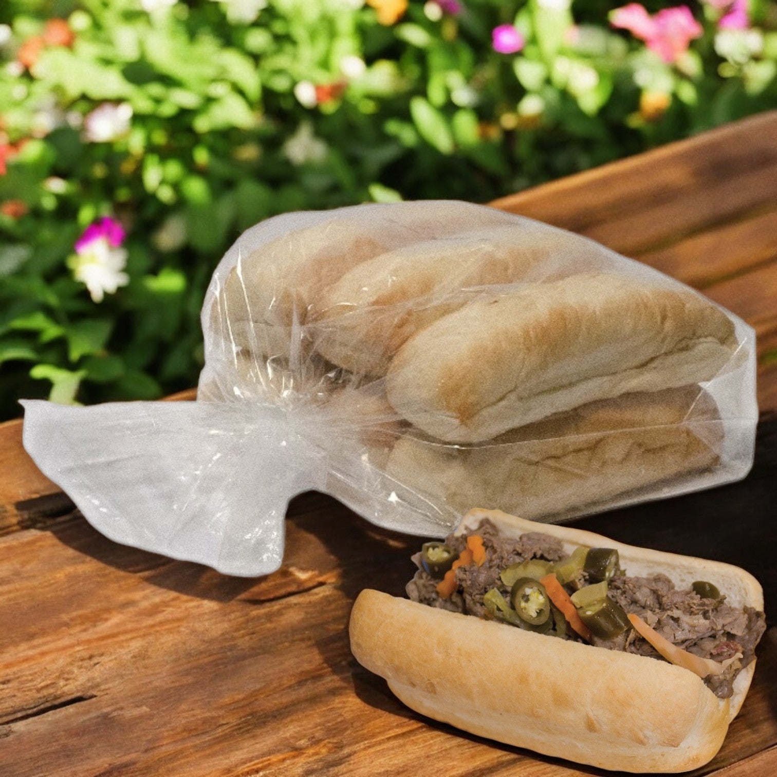 An Italian Beef Hoagie with jalapeños and veggies sits on a wooden table next to Easy Lunches' 6 Pack Hoagie Hearth Hinged 6" Buns. Flowers and greenery add a cozy touch in the background.